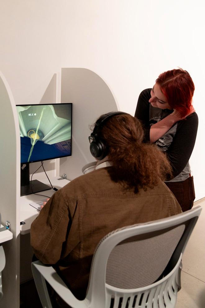 person sitting at computer with headphones on and someone standing instructing them