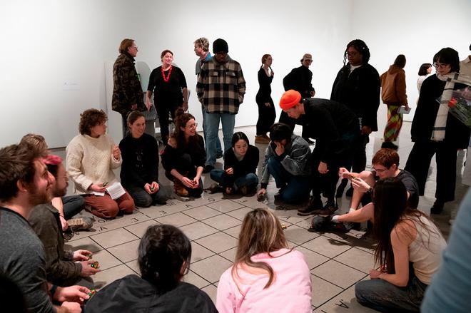 crowd forming a circle around a floor mat with small toy cars